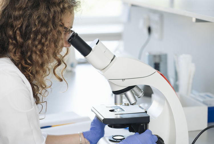 Scientist researching on sample through microscope in laboratory
