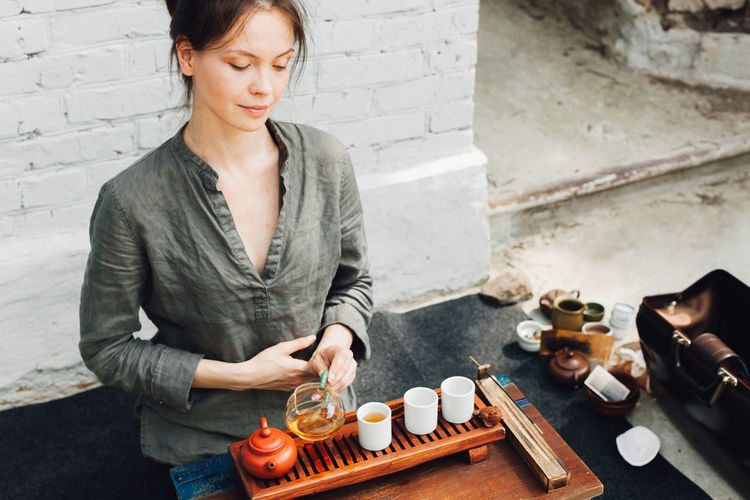Young woman preparing green tea while sitting against wall