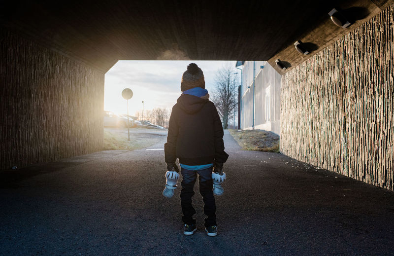 Young boy standing in a tunnel holding his ice skates in winter