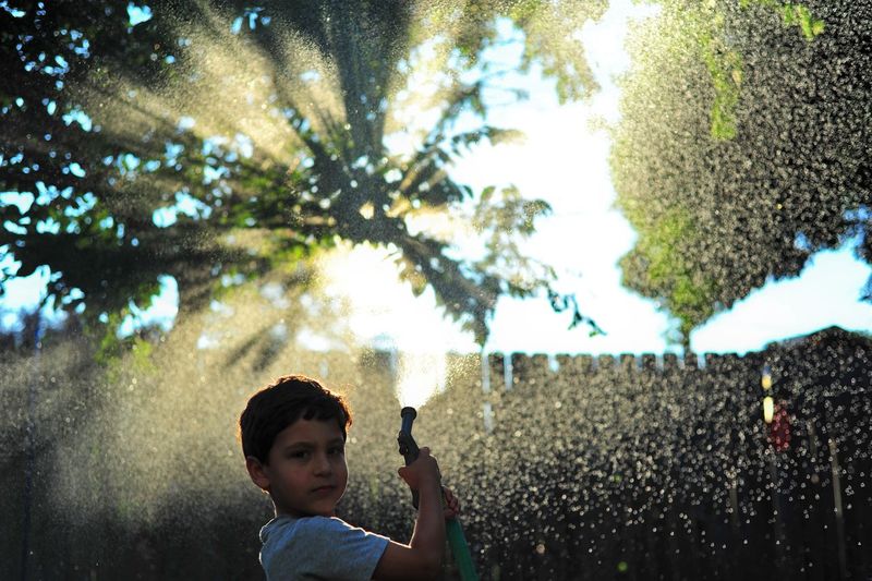 Boy standing by tree against water