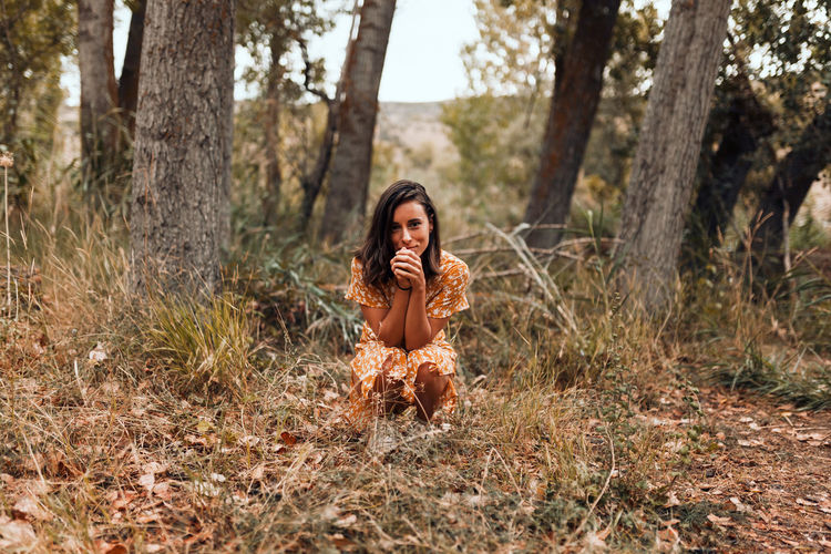 Portrait of young woman crouching on land in forest
