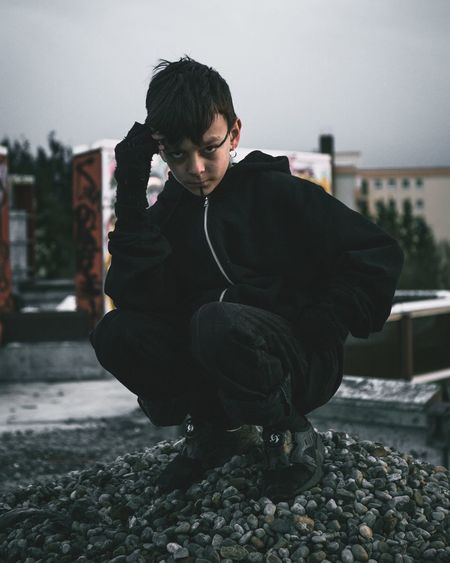 Full length portrait of boy crouching against building