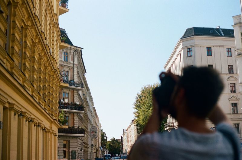 Rear view of man photographing buildings against sky