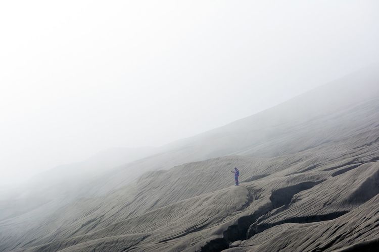 Low angle view of man standing on mt bromo in foggy weather against sky