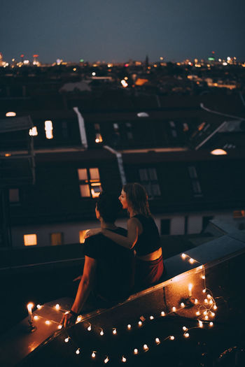 High angle view of couple sitting on illuminated terrace in city at dusk