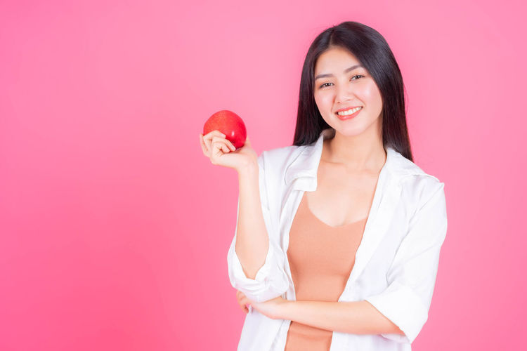 Smiling young woman holding apple against red background