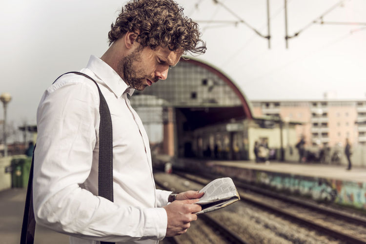 Side view of businessman reading newspaper on railroad station