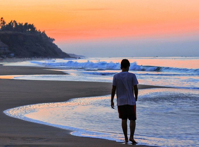 Rear view of man walking at beach during sunset