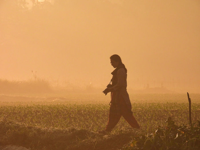 Side view of silhouette woman standing on field against sky during sunrise 