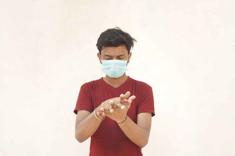 Young man wearing flu mask using hand sanitizer standing against white background