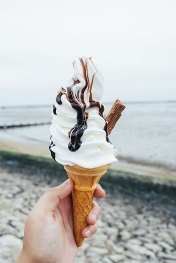 Close-up of hand holding ice cream cone at beach