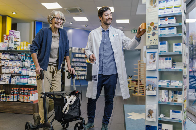 Smiling pharmacist and customer with wheeled walker in pharmacy