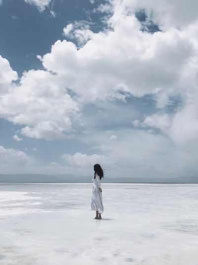 Woman standing at salt lake against cloudy sky