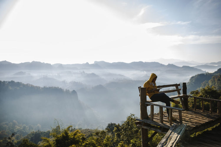 Man sitting on bench at observation tower against mountains