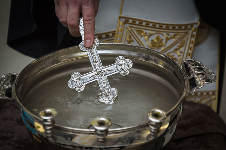 Midsection of priest pouring religious cross in holy water