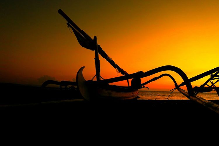 Silhouette outrigger moored at beach against clear sky during sunset