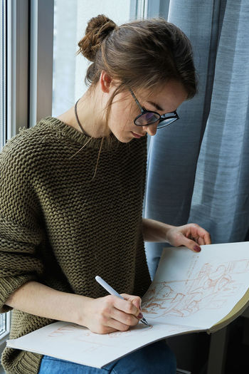 Millennial girl draws fabulous images on paper while sitting at home