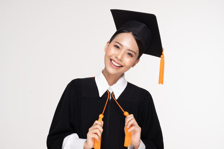 Portrait of young woman wearing mortarboard against white background