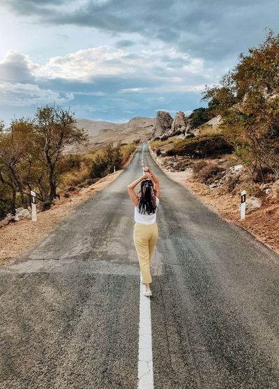 Rear view of young woman standing in middle of open road in summer.