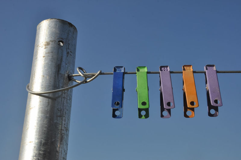 Low angle view of clothespins hanging on rope against blue sky