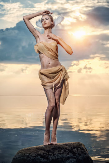 Woman standing at sea shore against sky during sunset