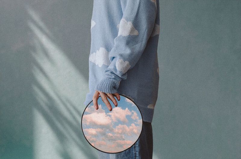 A man with a mirror in his hands reflecting the sky