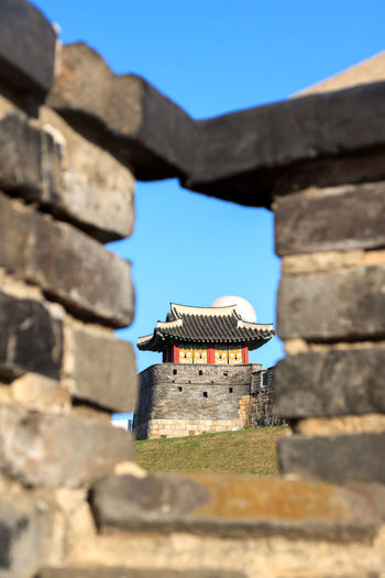 Low angle view of old korean guard tower building against blue sky framed by wall
