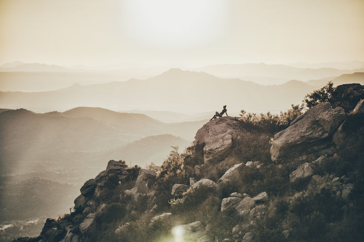 Mid distance view of woman sitting on rocks against mountains and clear sky