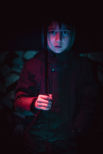 Portrait of young boy standing against wood background holding an umbrella