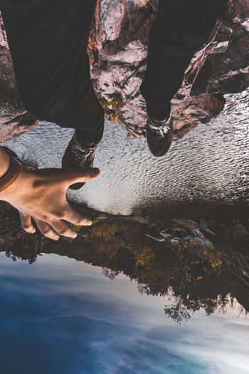 Upside down image of man sitting on rock by lake