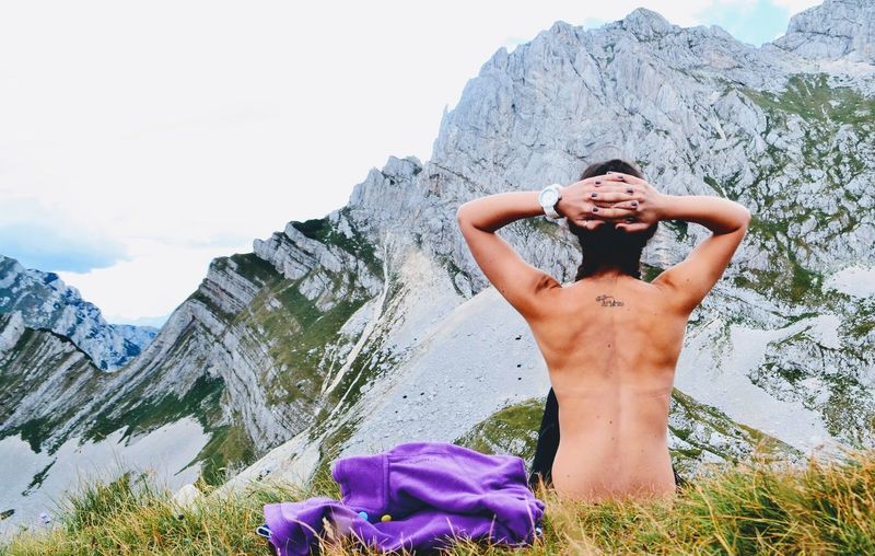 Shirtless woman sitting on field against mountains