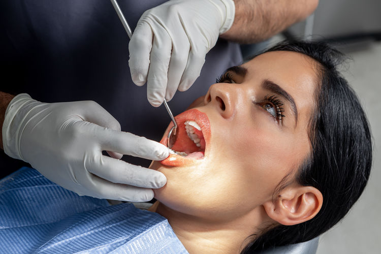 Female client with the mouth open while a dentist with gloves and tools examine her in a clinic