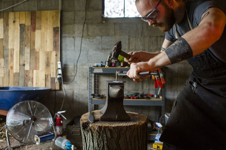 Blacksmith hammering knife on anvil in workshop