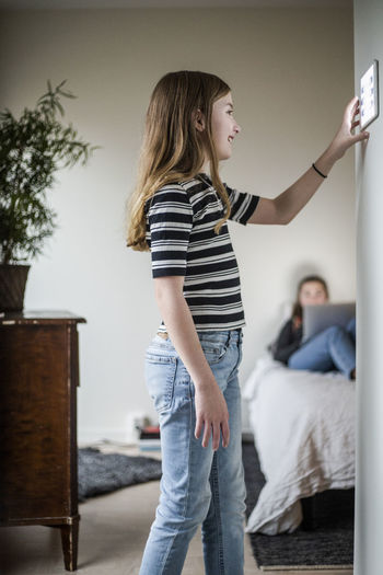 Girl using digital tablet on wall while sister sitting in background at modern home