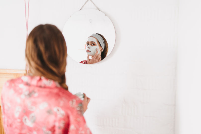 Woman applying facial mask while sitting at home