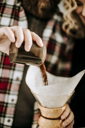 Man with flannel pours coffee grounds into pour over filter