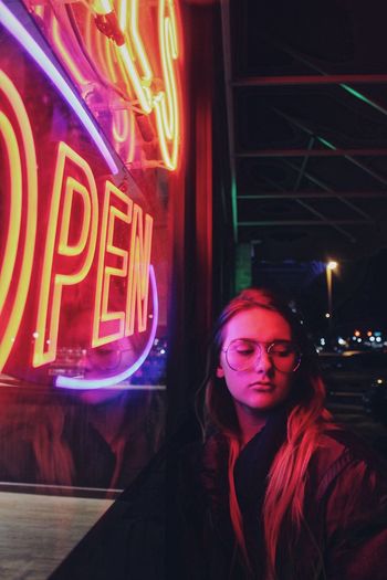 Young woman by illuminated neon lights at night