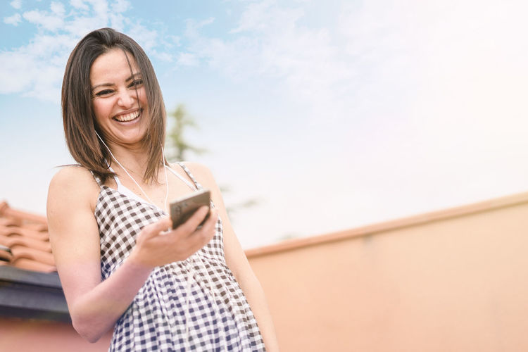 Portrait of smiling woman using mobile phone against sky