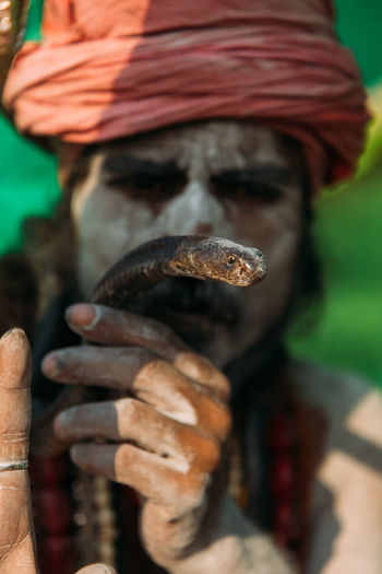 Varanasi, india - february, 2018: indian sadhu holy man with painted face and turban on head holding snake in hands