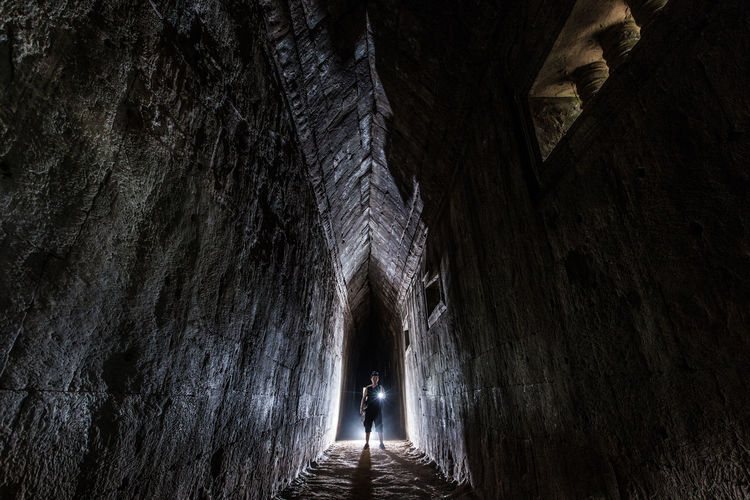 Man holding illuminated flashlight while standing in tunnel at angkor wat