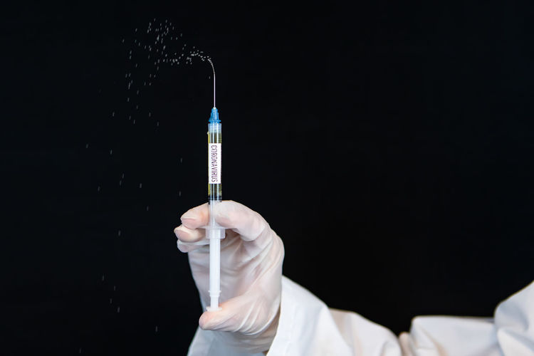 Cropped hand of doctor holding syringe against black background