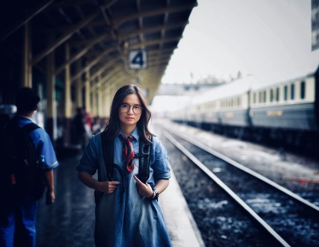 Portrait of smiling young woman standing at railroad station