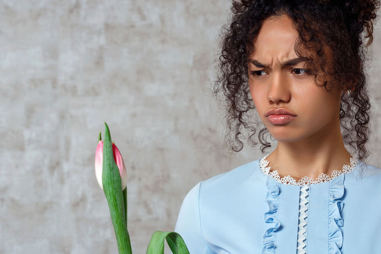 Woman holding tulip making face while standing against wall