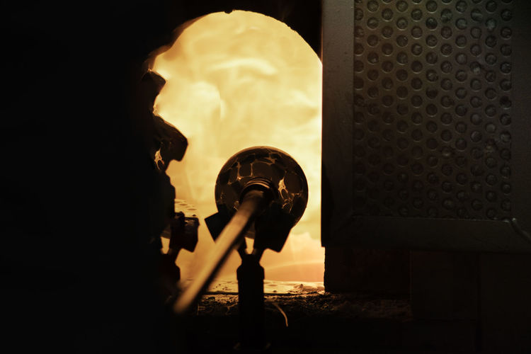 Close-up of glass blower by illuminated furnace