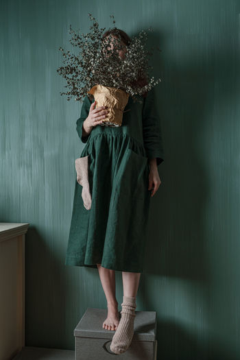 A young woman in a green linen dress making her creative self-portrait against a green wall