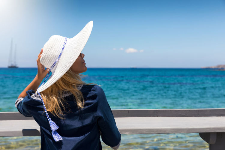 Rear view of woman wearing hat standing by sea against sky