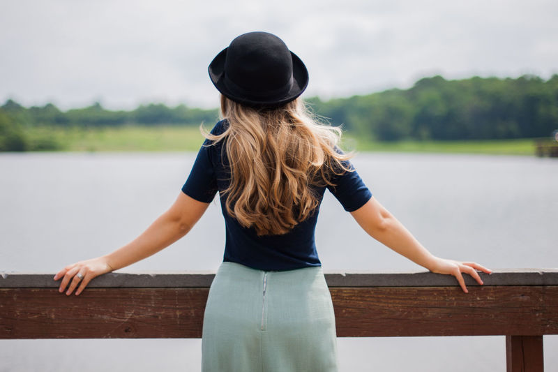 Rear view of woman with blond hair looking at lake while standing by railing