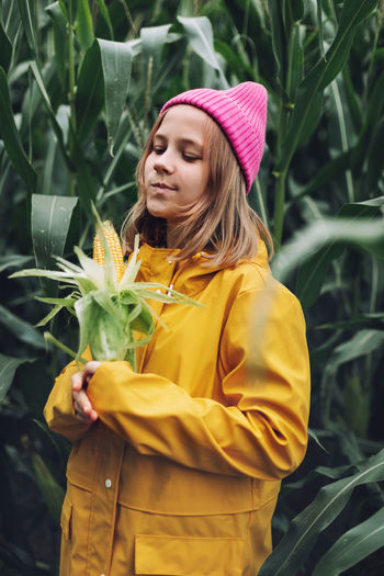 Funny little girl dressed in a yellow raincoat and a hot pink cap spoils and bites corn 