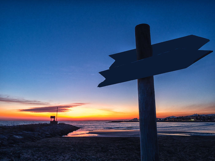 Silhouette cross on beach against sky during sunset