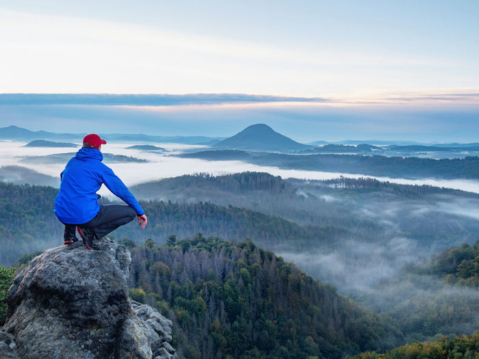 Sitting man on sharp rocky edge, enjoy amazing birds view. misty fall landscape bellow.